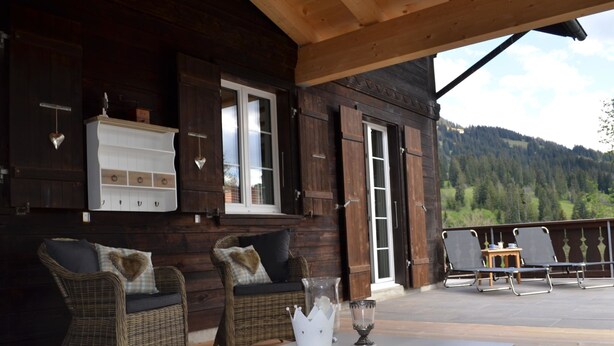 A wooden cabin with wicker furniture and a table with a vase and glass. - Apartment Ariel by Interhome (Saanenmöser)