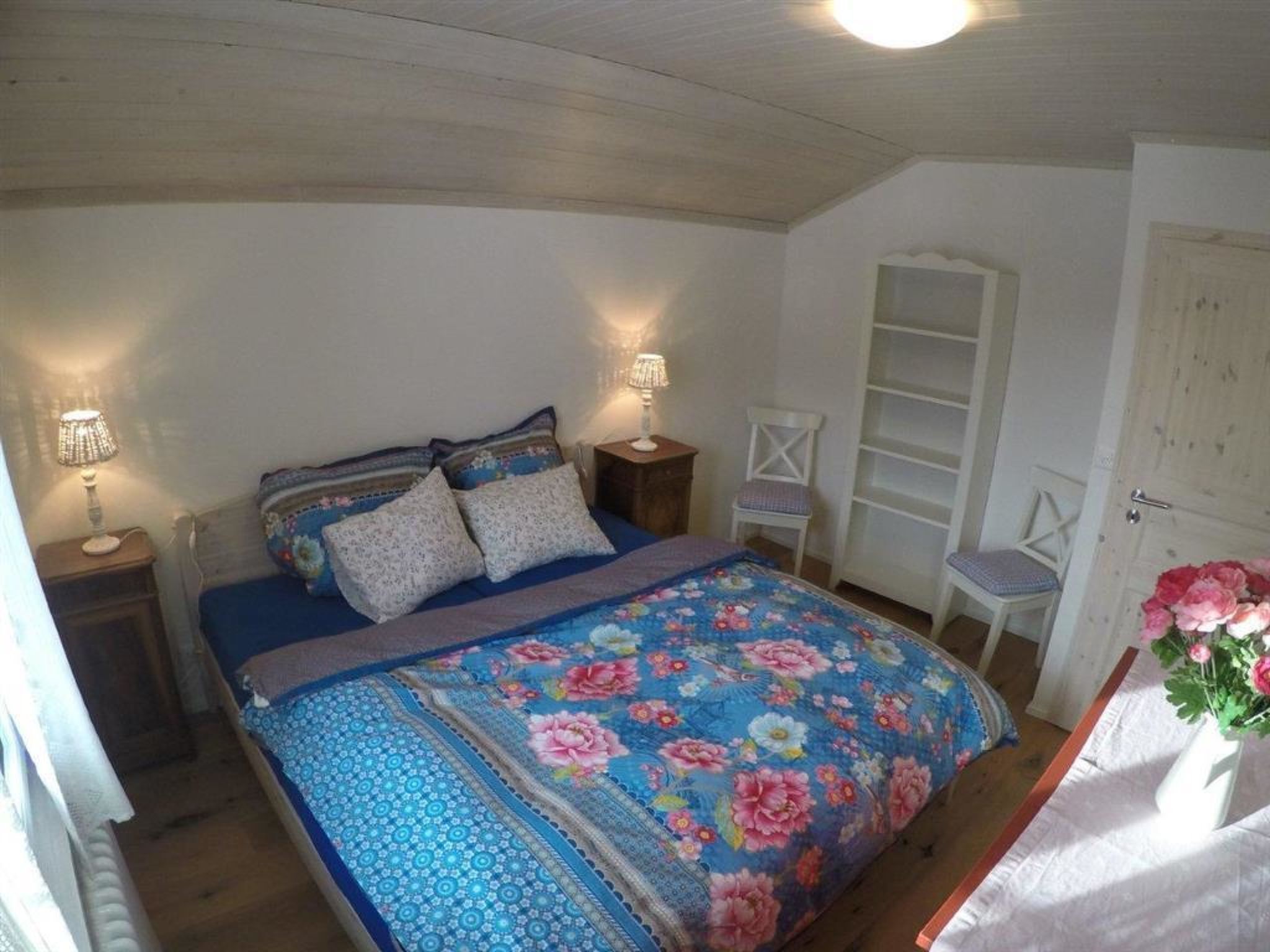 Quarto com cama, duas mesas de cabeceira, uma cadeira, guarda-roupa e porta.
