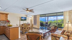 A spacious living area with a kitchen, dining area, and a balcony with a view. - Beachside Maui condo - pool & hot tub (Kihei)