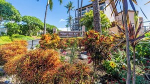A sign for 'Kihei Alii Kai' with a lush garden and palm trees. - Beachside Maui condo - pool & hot tub (Kihei)