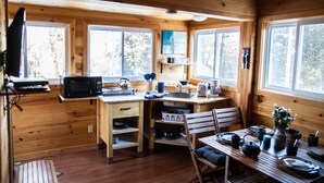 Une petite cabane en bois comprenant un coin cuisine équipé d’un four à micro-ondes, d’un évier et d’une table à manger pour quatre personnes.