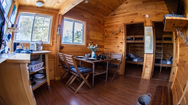 L’intérieur chaleureux d’un chalet comprend un coin repas en bois, une cuisine avec un évier et un plan de travail, ainsi que deux espaces nuit dotés de lits encastrés.