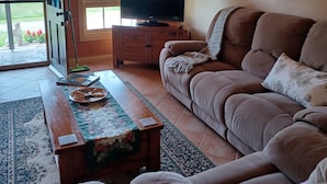 A cozy living room with a brown sofa, a television on a wooden stand, a patterned rug, and a door leading outside.