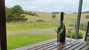 A wooden table with two wine glasses and a bottle of wine, overlooking a vineyard.