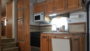 Cozinha compacta com armários de madeira, micro-ondas, fogão e geladeira.