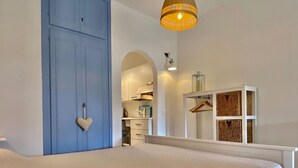 A bedroom with a large blue door, a hanging heart decoration, a white bedside table, and a wardrobe with a wicker basket. - Portolano - Portolano 6 (Porto Azzurro)