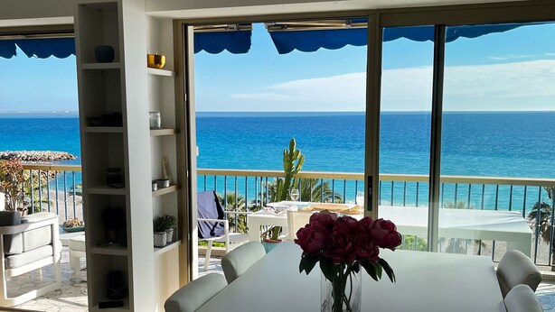 A modern dining area with a large table, a vase with flowers, and a view of the ocean.