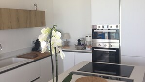 A modern kitchen with white cabinetry, a built-in oven, and a central island with a plant.
