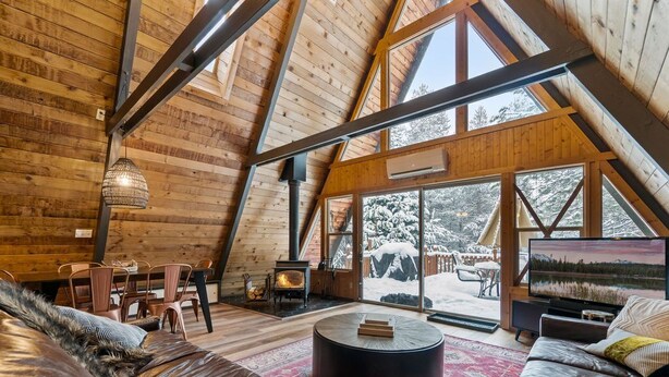 Ein gemütlicher Holzraum mit hohen Decken, einem Kamin, einer Sitzecke und großen Fenstern mit Blick auf eine verschneite Landschaft.
