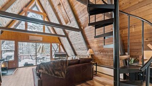 Ein geräumiges Loft mit hoher Decke, Holzbalken, einer Wendeltreppe, einem Ledersofa und Blick auf eine verschneite Terrasse.