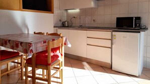 Uma cozinha compacta com uma mesa de jantar, cadeiras, micro-ondas, mini-geladeira e um armário de madeira sobre o balcão.