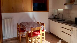 Uma cozinha pequena com armários de madeira, uma mesa com cadeiras e um radiador.