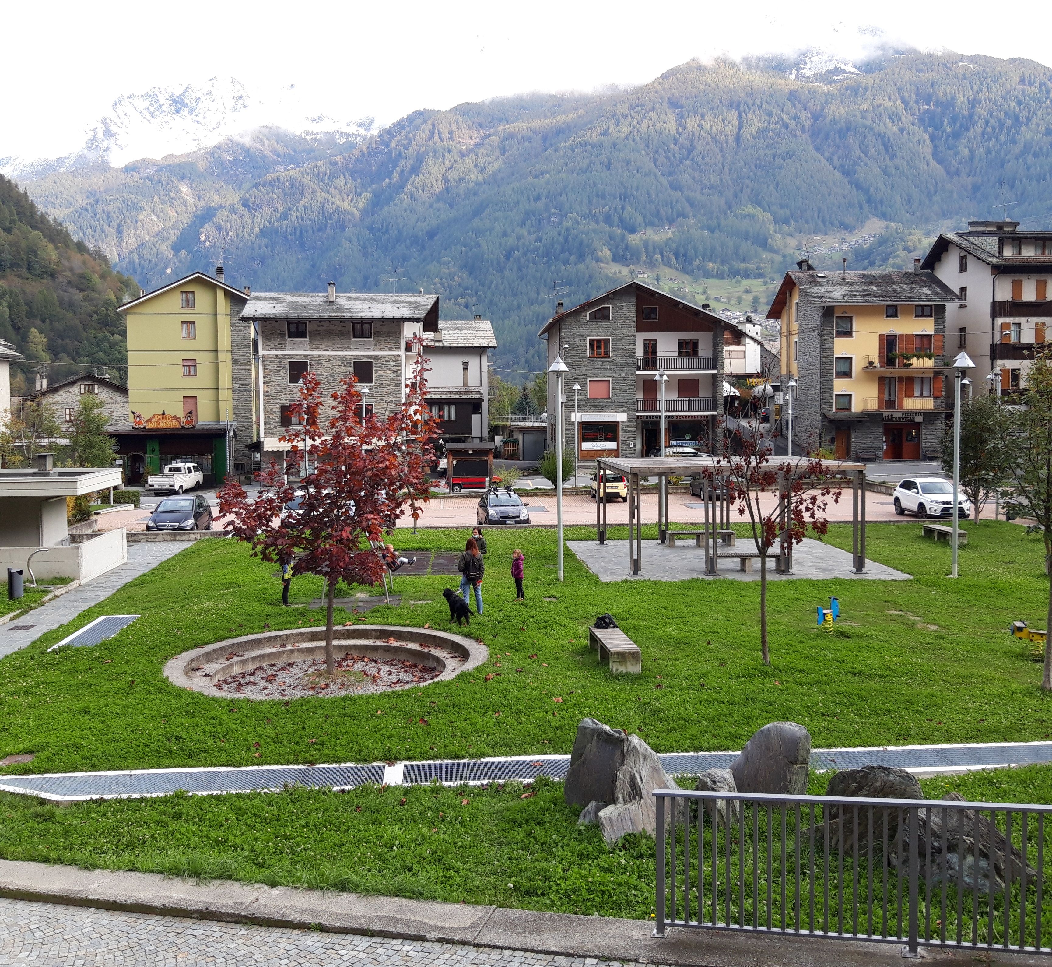 A residential area with houses, a central park with a tree, and a mountain backdrop.