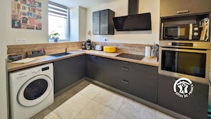 A modern kitchen with a built-in washer, a microwave, and a large window with blinds. - "Charming Cottage with Private Observatory, Terrace & Garden in Origné" (Origne)
