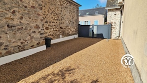 A courtyard with a gravel path, stone walls, and a metal gate. - "Charming Cottage with Private Observatory, Terrace & Garden in Origné" (Origne)