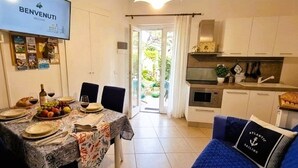 A dining area with a table set for four, a kitchen with white cabinets, and a blue sofa with a pillow. - "CASA POMONTE" ON THE SEA with PRIVATE PARKING SPACE. (Pomonte)