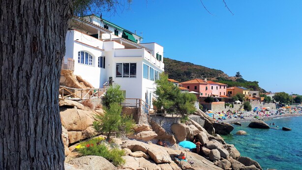 A coastal building with a balcony, a rocky shoreline, and a beach with umbrellas. - "CASA POMONTE" ON THE SEA with PRIVATE PARKING SPACE. (Pomonte)