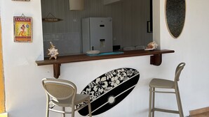 Zona de bar con dos taburetes, una decoración con tabla de surf y carteles antiguos en la pared.