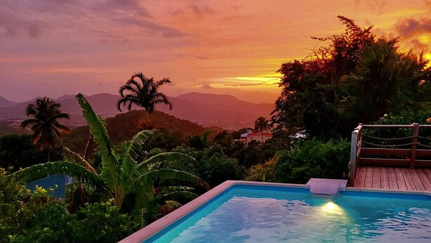 Piscina con muelle de madera y vista a montañas al atardecer.