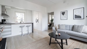 A modern kitchen with white cabinets, a central island with stools, and a dining area with a grey sofa and a round black table. - 1BR Penthouse with Sauna & Private Rooftop Terrace (Tampere)