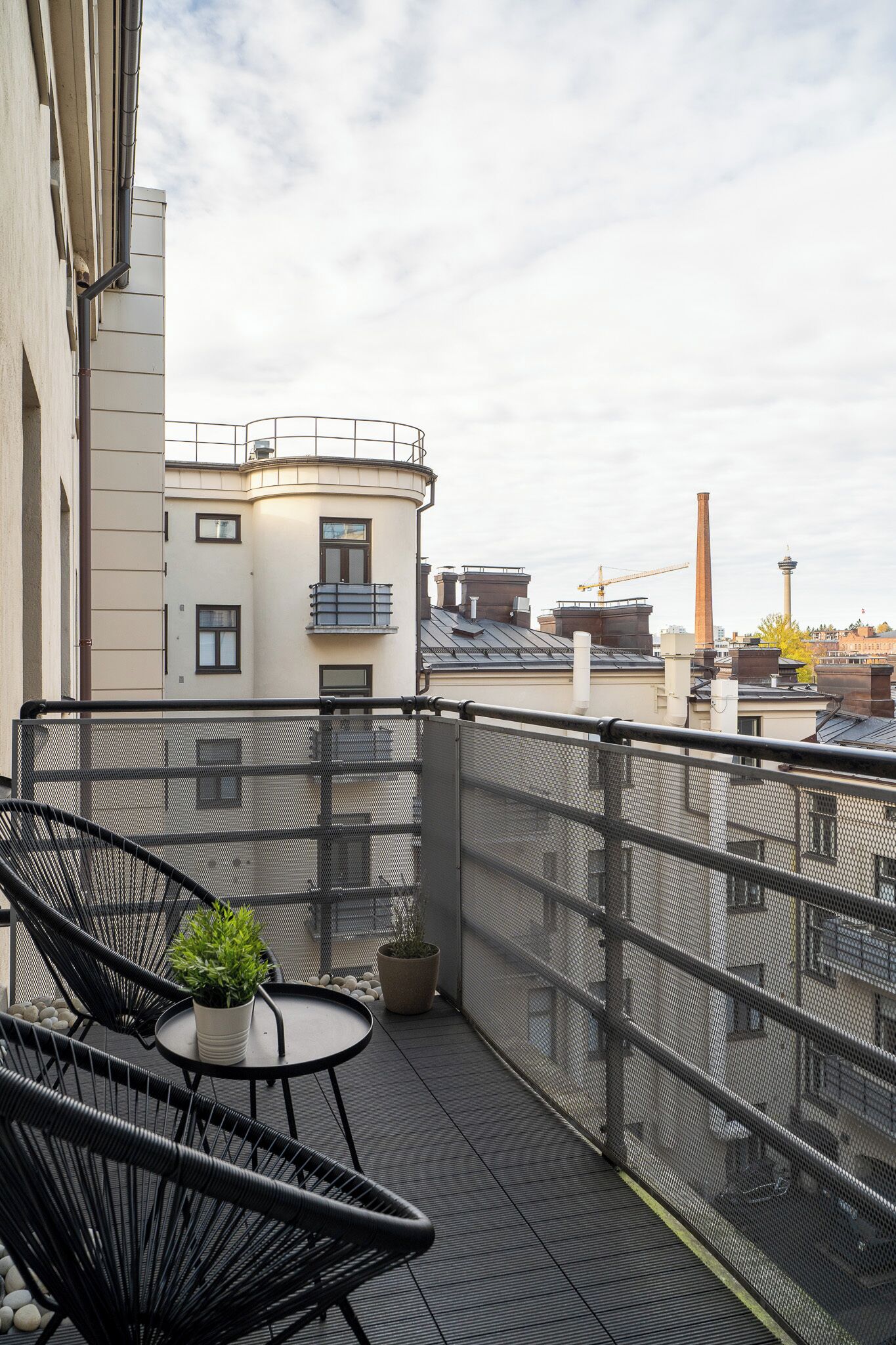 Una terraza en la azotea con barandilla metálica, una mesita con planta en maceta y dos sillas negras.