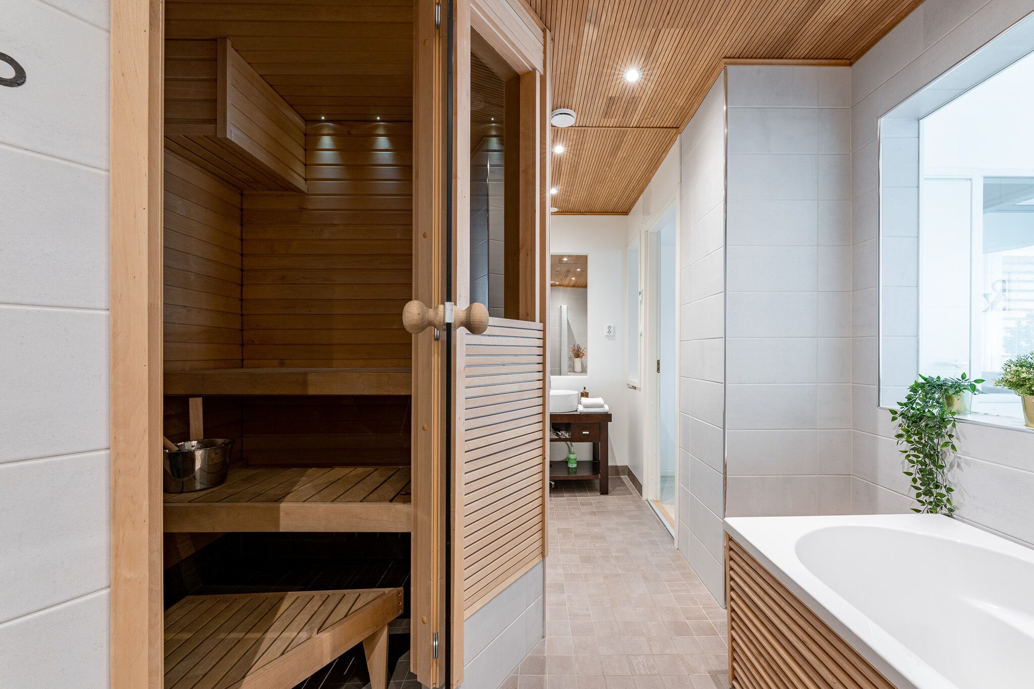 Un baño moderno con sauna de madera, bañera y una pequeña zona de lavamanos.