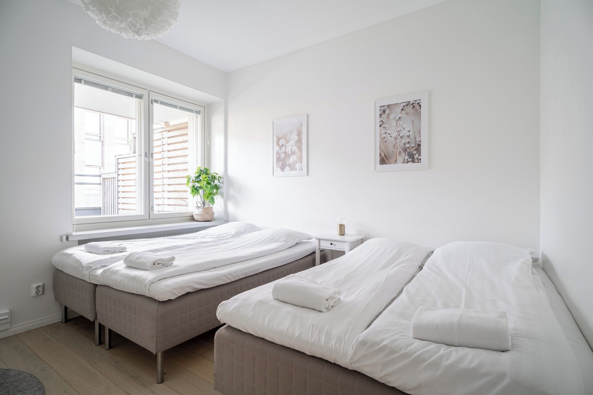 Une chambre à coucher propre et moderne, avec deux lits, une fenêtre avec des stores, une table de chevet avec une lampe et des œuvres d’art murales.