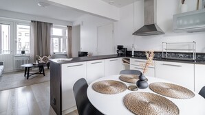 A modern kitchen with white cabinetry, a central island, and a dining area with a round table and chairs. - 1BR Penthouse with Sauna & Private Rooftop Terrace (Tampere)