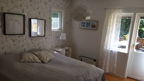Un dormitorio con una cama, una mesita de noche, una lámpara, cuadros enmarcados, una ventana y vistas al exterior.