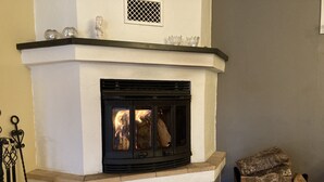 Una chimenea con repisa blanca y marco negro, leña en una cesta, y un adorno metálico en la repisa.