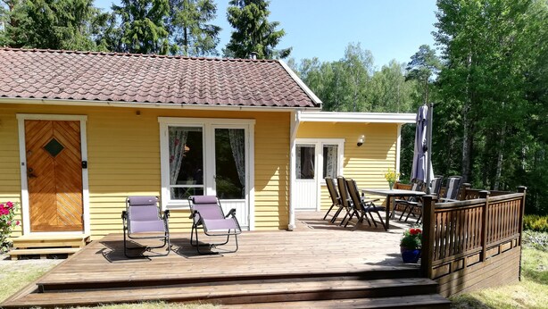 Una casa amarilla con un porche de madera, un patio techado y mobiliario exterior.