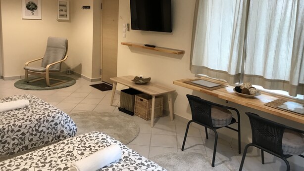 A room with two beds, a chair, a desk, a television, and a window with curtains. - Flight Apartment Airport (Spata-Artemida)
