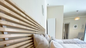 A hotel room with a wooden headboard, a bed with white bedding, and a patterned throw pillow. - Flight Apartment Airport (Spata-Artemida)