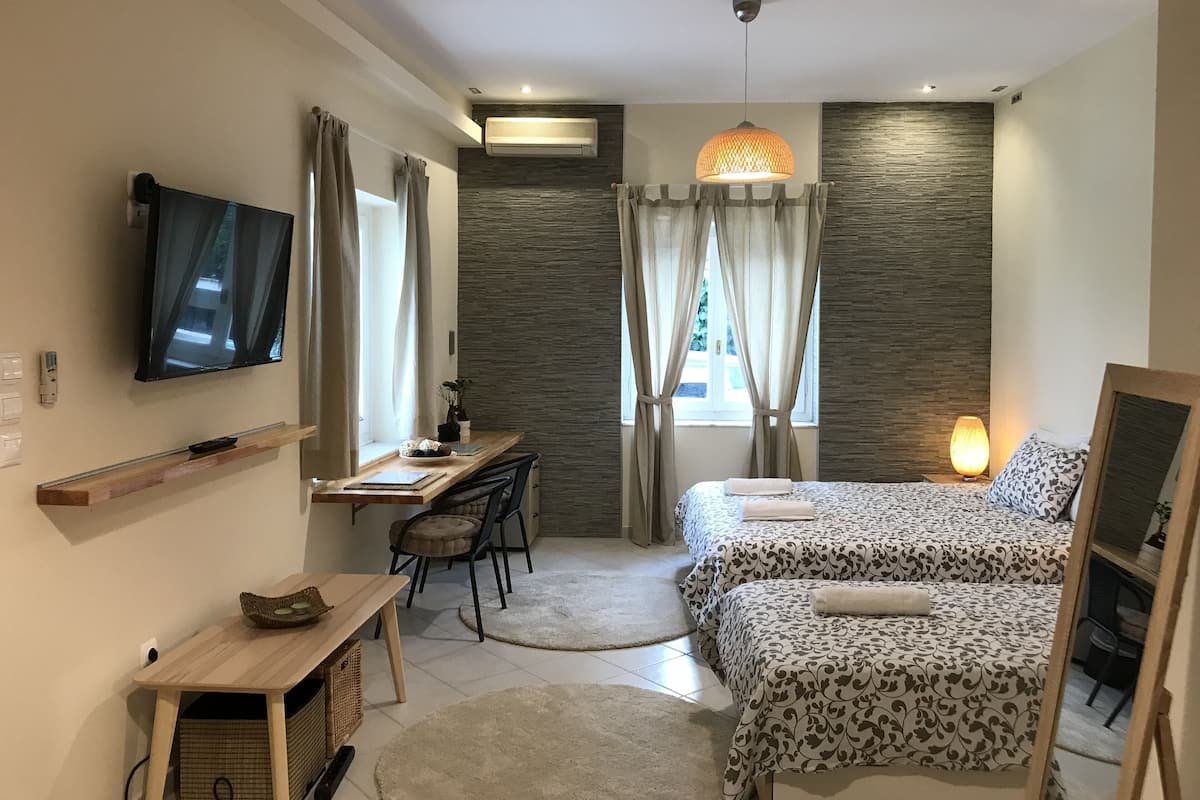 Un dormitorio moderno con cama, escritorio, silla, televisor y ventana con cortinas.
