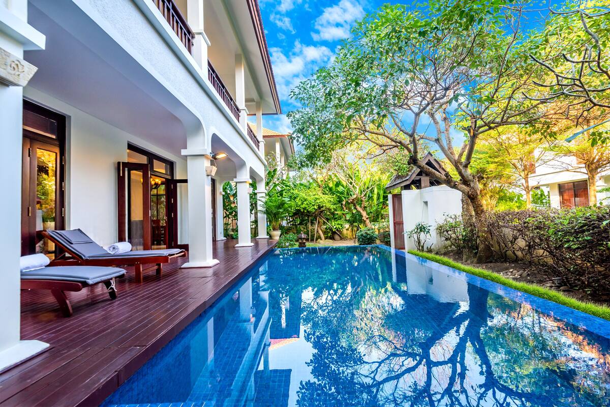 A swimming pool with lounge chairs and a white building with balconies.