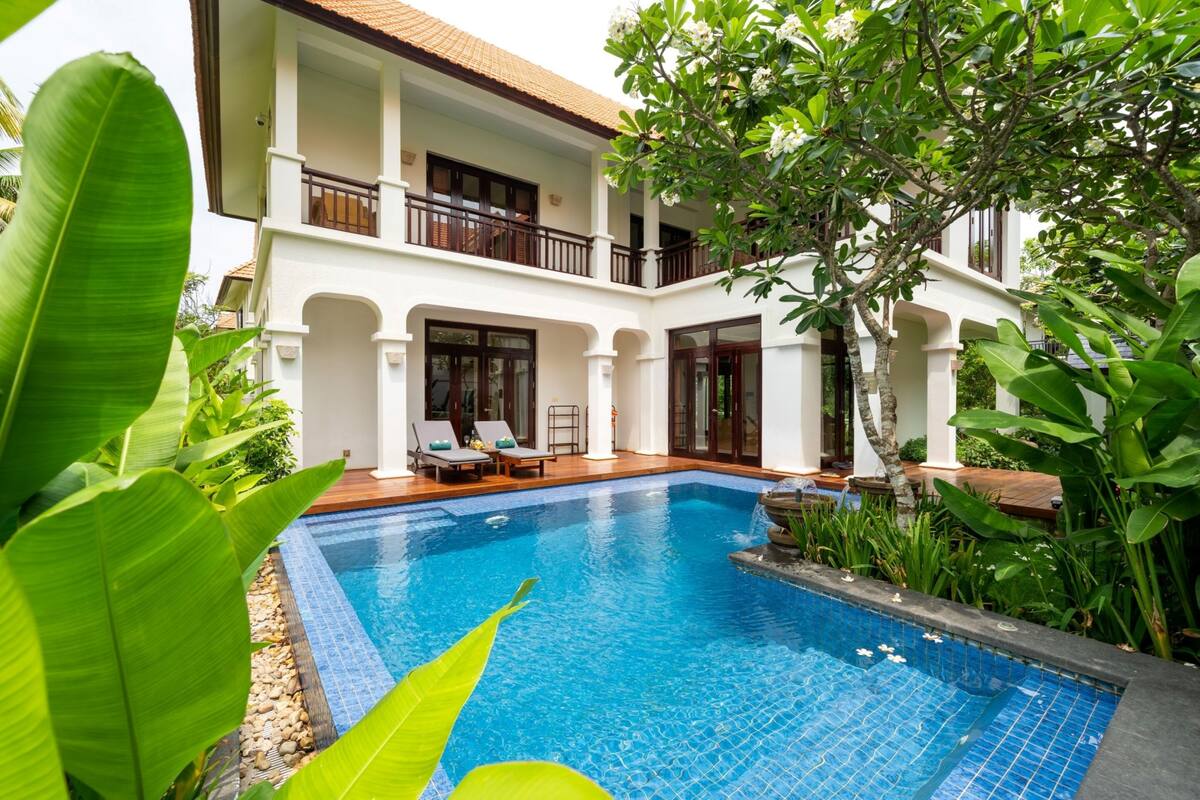 A two-story building with a swimming pool, surrounded by lush greenery.