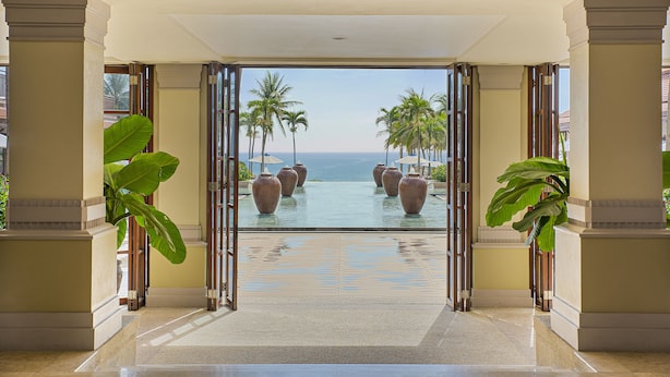 A hotel entrance with a view of a pool and palm trees.