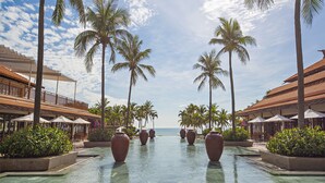 A pool area with palm trees, umbrellas, and a view of the ocean.