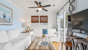 Un salon avec un canapé blanc, une table basse en bois, un ventilateur de plafond et un téléviseur posé sur un meuble en bois.