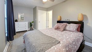 A bedroom with a bed, a ceiling fan, a dresser, a mirror, and a door. - Calm and cozy WV home conveniently located. (Teays Valley)