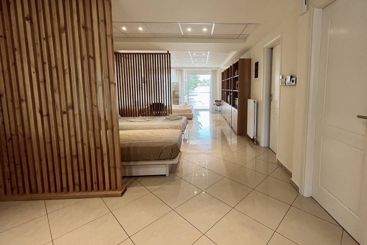 A hotel room with a bed, a wooden partition, a bathroom with a toilet and sink, and a hallway with a door.