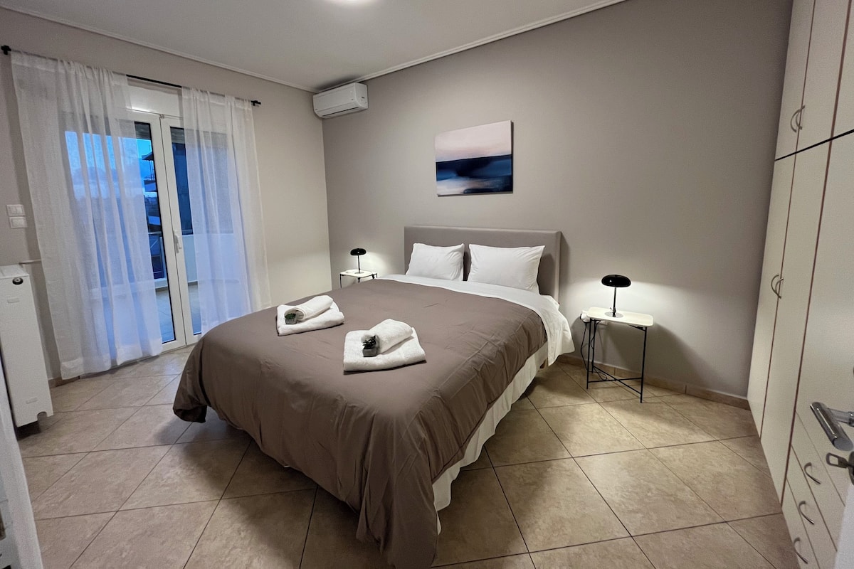 Habitación de hotel moderna con una cama grande, dos mesitas de noche, una lámpara en el techo y vistas al exterior a través de una puerta corrediza.