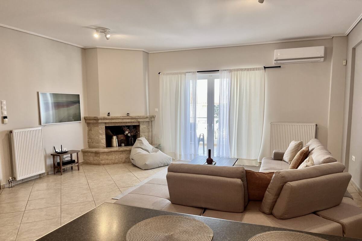 A modern living room with a fireplace, a sofa, a coffee table, and a view of the outdoors.