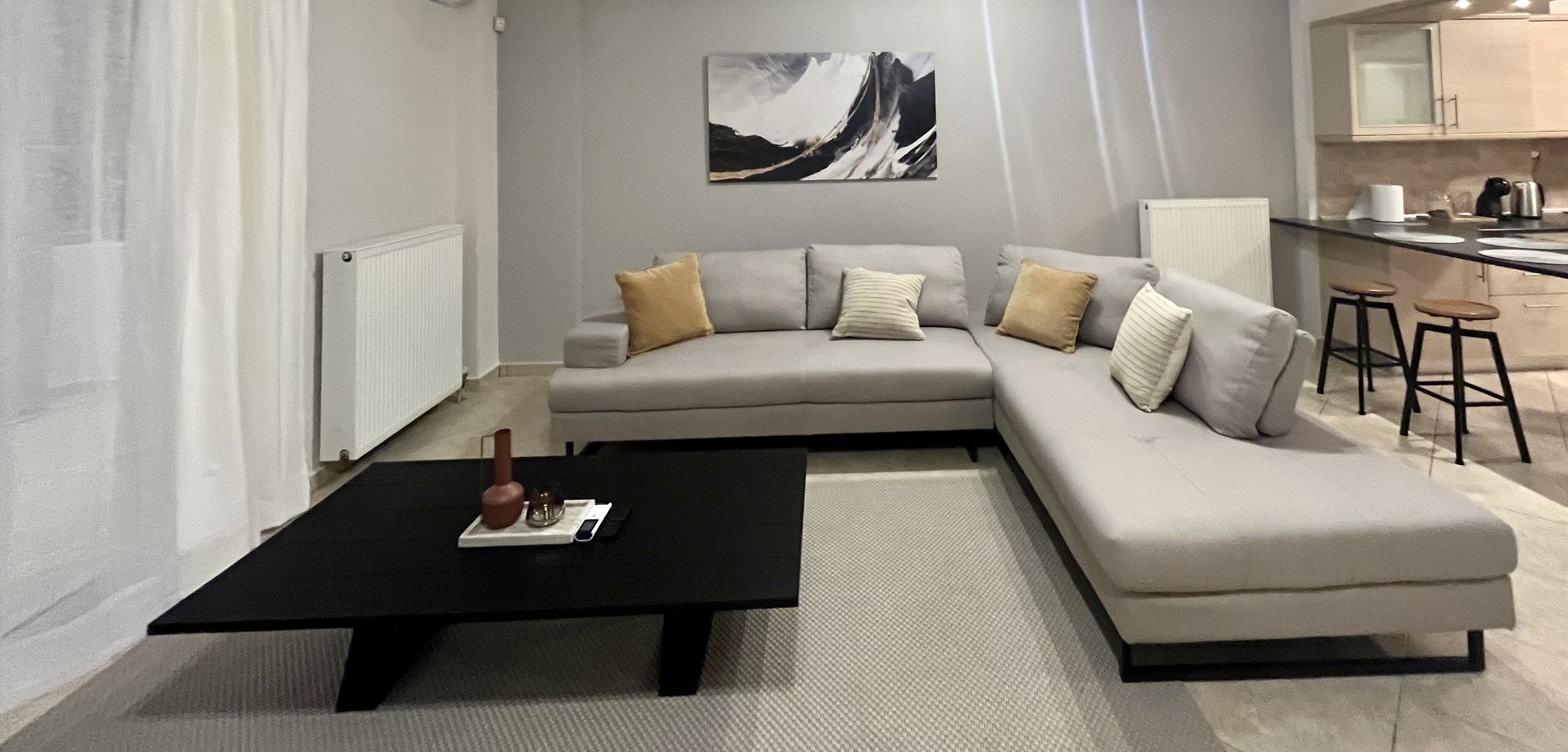 A modern living room with a grey sectional sofa, a black coffee table, and a kitchen area in the background.
