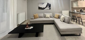 Una sala de estar moderna con un sofá seccional gris, una mesa de centro negra y una cocina al fondo.