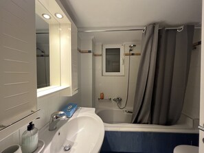 Casa de banho com uma pia branca, um espelho, chuveiro e banheira.