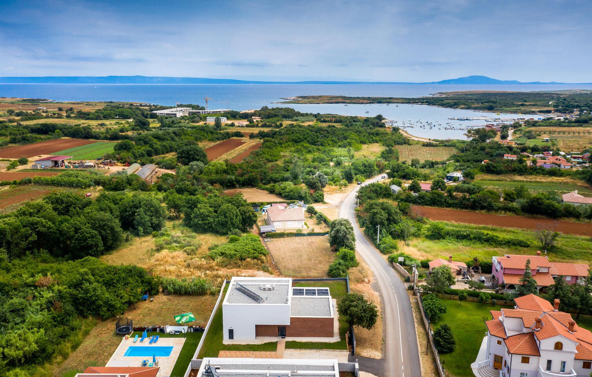 Vista aérea de una zona costera con una carretera, campos verdes y edificios residenciales.
