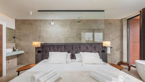 Una habitación de hotel moderna con una cama grande, dos mesitas de noche, ducha integrada y un ventanal amplio.