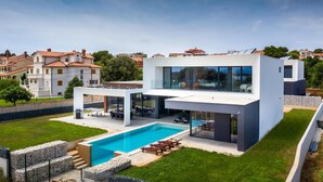 Una casa moderna de dos pisos con piscina, amplios ventanales y techo plano.
