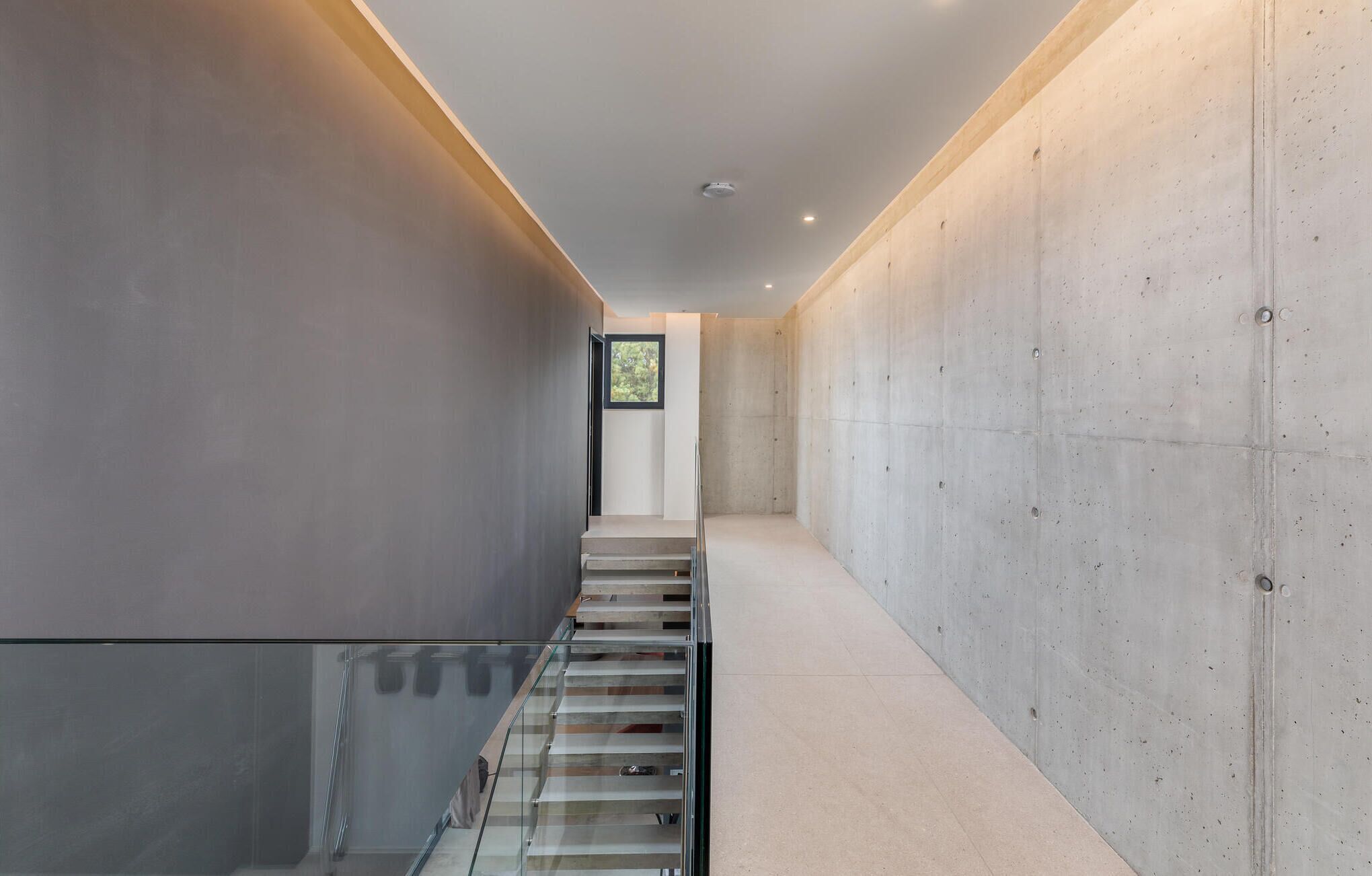 A modern interior with a glass staircase, concrete walls, and a ceiling light fixture.